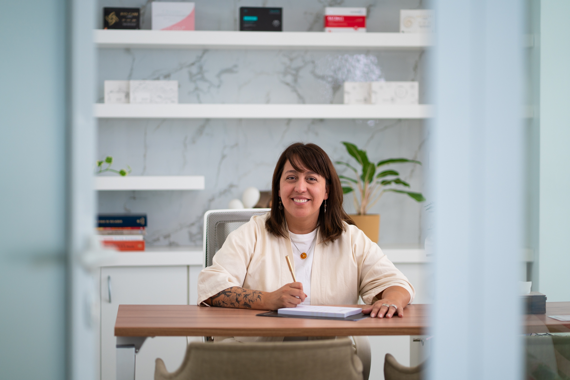Claudia sonriendo en su escritorio del consultorio, vista desde la puerta